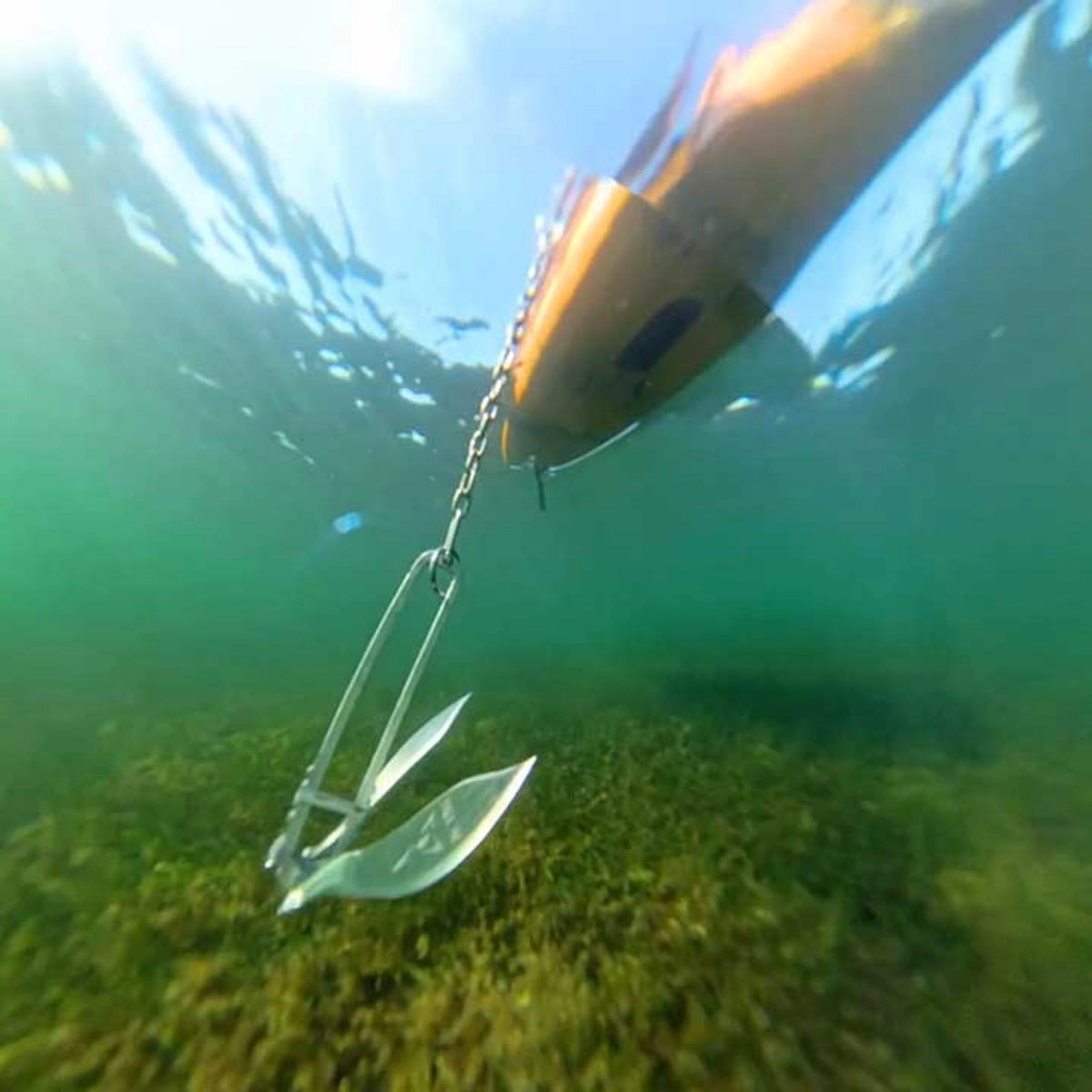 Active Anchors DF200 kayak anchor suspended underwater by its chain above a seagrass-covered seabed beneath a kayak.