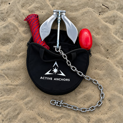 Active Anchors DF200 boat anchor with chain emerging from an open black storage bag, alongside coiled rope and a red float on sand.