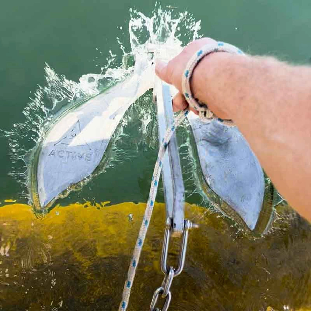 Active Anchors DF300 releasable boat anchor held at the water's surface beside a kayak, showing its curved metal flukes.