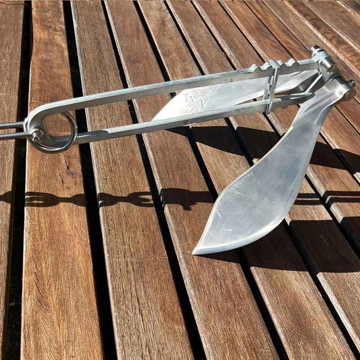 Side view of the Active Anchors DF300 folding boat anchor on wooden decking, showing its curved flukes and galvanised steel shank.