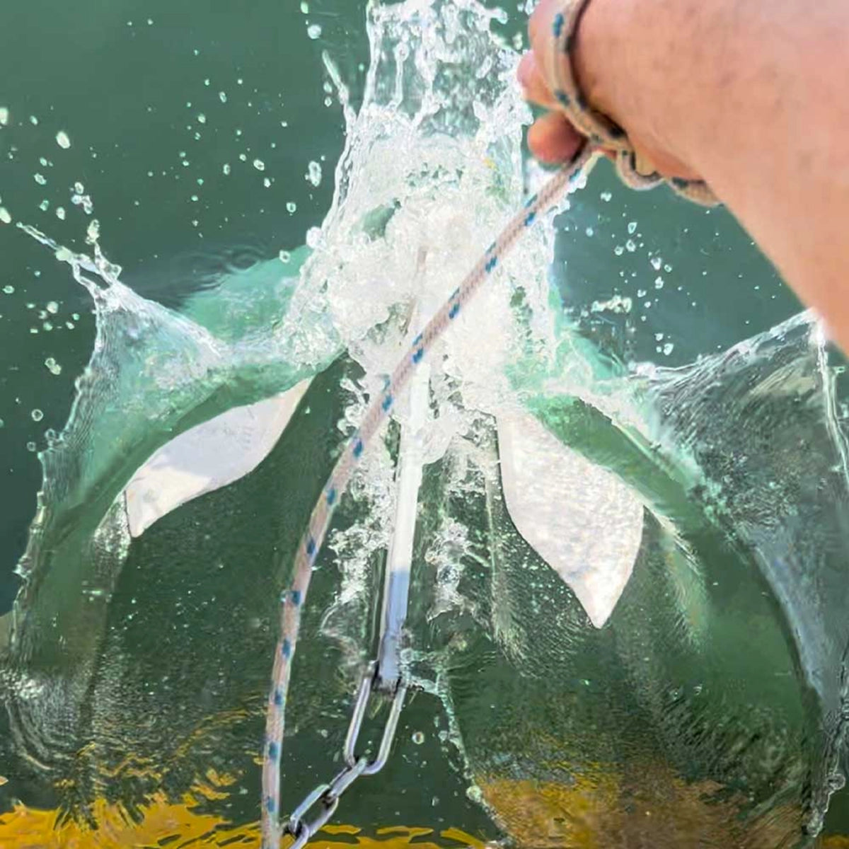 Active Anchors DF400 releasable boat anchor being lowered into the water by rope, showing its curved stainless steel flukes.
