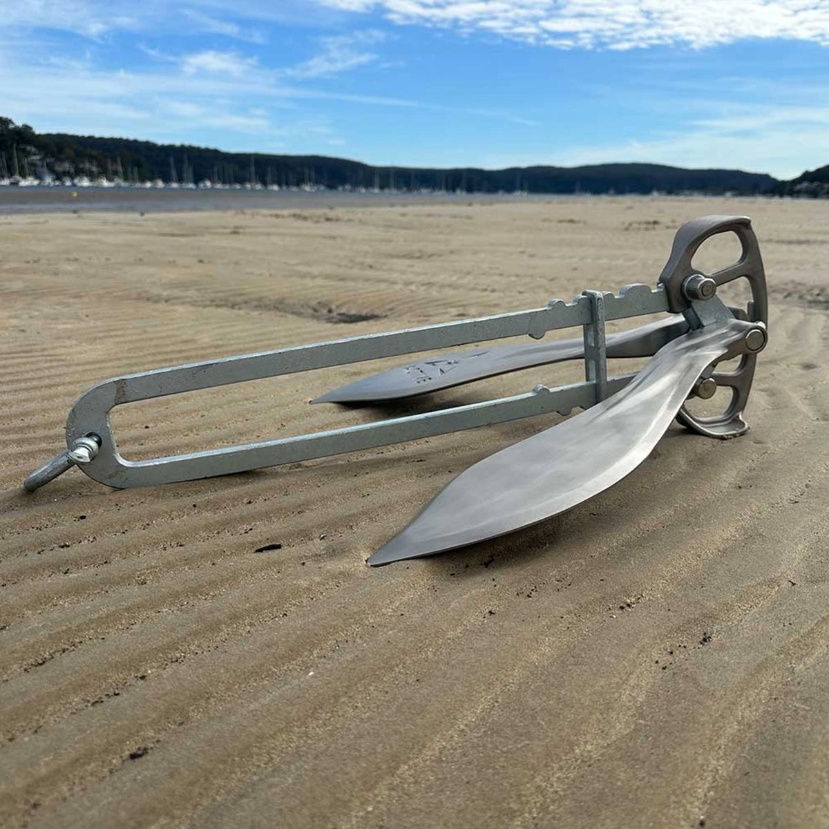 Side view of the Active Anchors DF600 marine anchor resting on a sandy beach, showing its stainless steel flukes and long galvanised shank.