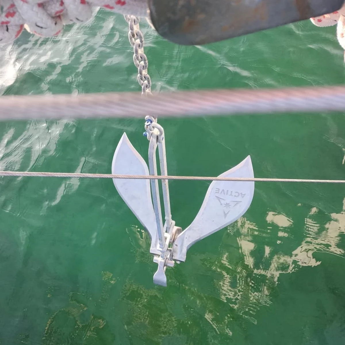 Active Anchors DF600 releasable boat anchor suspended by a metal chain above green seawater, showing its wide curved stainless steel flukes.