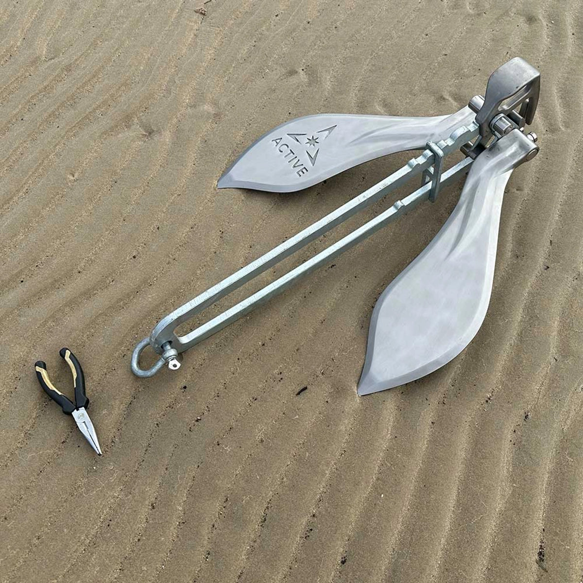 Active Anchors DF600 releasable marine anchor laid on sand with twin stainless steel flukes, galvanised shank and pliers alongside.