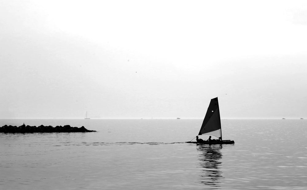 Black and white image of a sail boat in the middle of the sea.